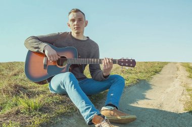 Elinde gitarla genç bir adam. Doğada bir gitarla dinlenmek.