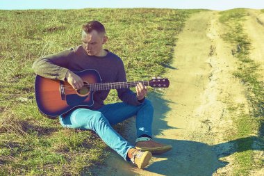 Genç bir adam gitar çalar. Patikada otur ve oyna.