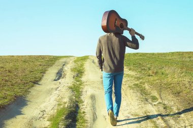 Omzunda gitar olan bir adam yol boyunca gider.