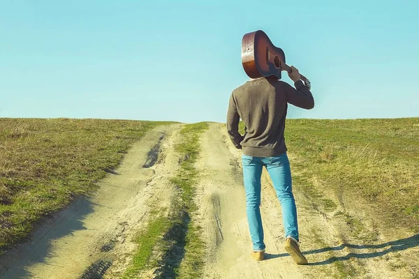 Omuzlarında gitarla yolda duran bir adam.