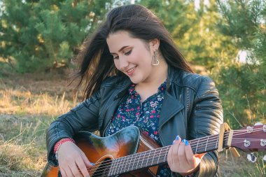 Kız gitar çalarken gülümsüyor. Açık havada dinlen.