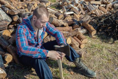 Oduncu dinleniyor. Elinde balta olan genç bir adam.