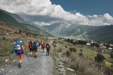 Büyük sırt çantalı bir grup turist Kafkasya Dağları 'ndaki karlı tepelere tepeden bakan çimenli yamaca tırmanıyor.