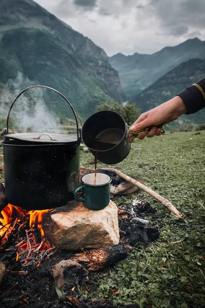 Koyu büyük tencere ya da kazan, ateşin içinde kaynar suyla pişirme tavası, parkta ya da dağlarda bir yerde, kamp konsepti.