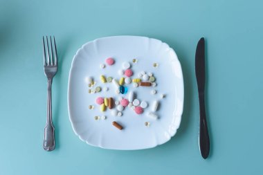 Çatal bıçak takımının yanındaki tabakta bir avuç dolusu hap, kapsül ve çok renkli tabletler. İlaç alıyorum. Yemek yerine hap. Yiyecek yerine vitamin konsepti