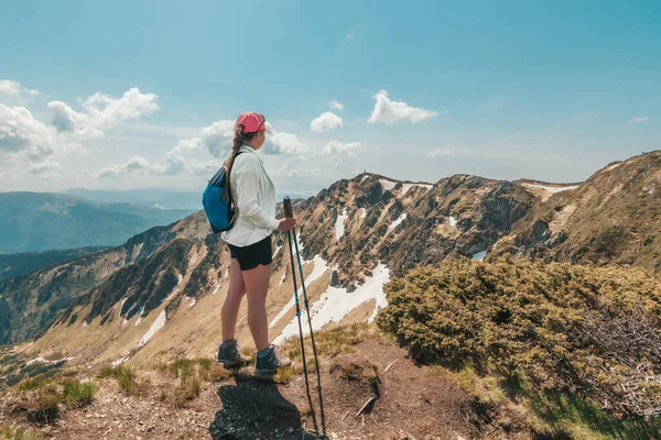 Sırt çantalı bir kız dağlarda bir kayanın üzerinde duruyor. Hayatı dolaştım. Karpatlar 'ın dağlarında yürüyüş. Yeşil dağ yamaçları ve çiçek açan rhododendron.
