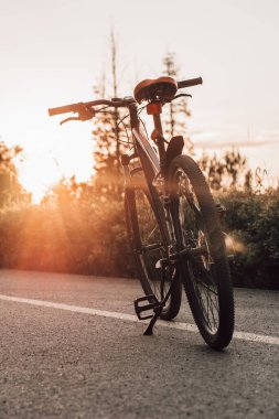 Şehir parkındaki fayanslı yolda yaz günbatımında bisiklet. Bulanık yaz arkaplanındaki bisiklet yakın çekim tekerleği. Yaz günbatımında işe bisikletle gitmek. Bisiklet ve ekoloji yaşam tarzı kavramı.