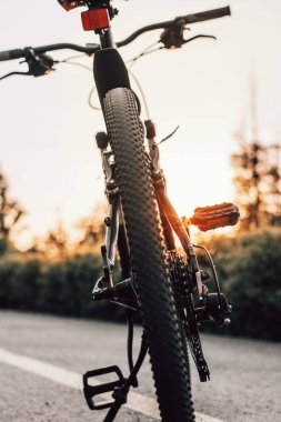 Şehir parkındaki fayanslı yolda yaz günbatımında bisiklet. Bulanık yaz arkaplanındaki bisiklet yakın çekim tekerleği. Yaz günbatımında işe bisikletle gitmek. Bisiklet ve ekoloji yaşam tarzı kavramı.