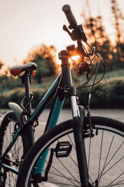 Şehir parkındaki fayanslı yolda yaz günbatımında bisiklet. Bulanık yaz arkaplanındaki bisiklet yakın çekim tekerleği. Yaz günbatımında işe bisikletle gitmek. Bisiklet ve ekoloji yaşam tarzı kavramı.