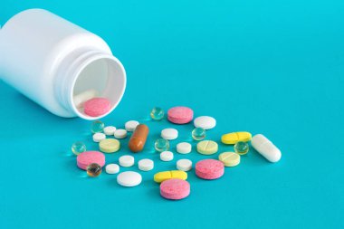 Bir ilaç şişesinden birçok hap dökülür. Mavi arka planda haplar ve haplar. Tıbbi haplar: ağrı kesici, antipiretikler