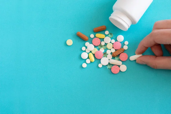 Bir ilaç şişesinden birçok hap dökülür. Mavi arka planda haplar ve haplar. Tıbbi haplar: ağrı kesici, antipiretikler