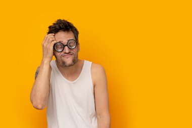 Komik miyop adam, kalın gözlükler takıyor, gözleri kapalı ve düşünceli bir yüz ifadesi var.