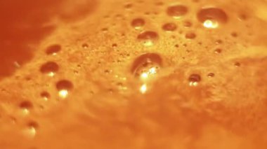 Foam with bubbles on surface of boiling cocoa, coffee chaotically rotating close-up at high angle.