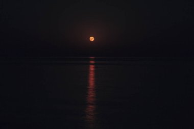 Dolunay, durgun denizin üzerindeki karanlık bir gecede gökyüzünde ışıldıyor. Su üzerindeki güzel ay yolu