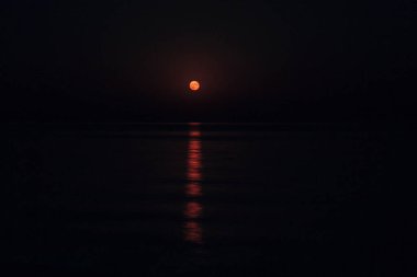 Dolunay, durgun denizin üzerindeki karanlık bir gecede gökyüzünde ışıldıyor. Su üzerindeki güzel ay yolu