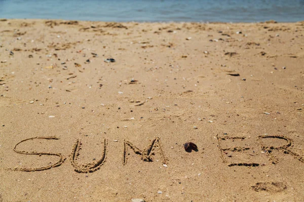 Texto de verano escrito en la arena de una playa. El mar sobre un fondo de letras —  Fotos de Stock