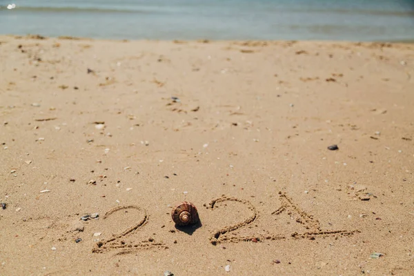 Texto 2021 Escrito en la arena de una playa. El mar sobre un fondo de letras —  Fotos de Stock