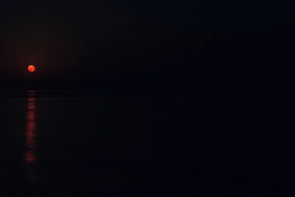 Plný rudý měsíc jasně svítí na obloze za temné noci nad klidným mořem s kopírovacím prostorem — Stock fotografie