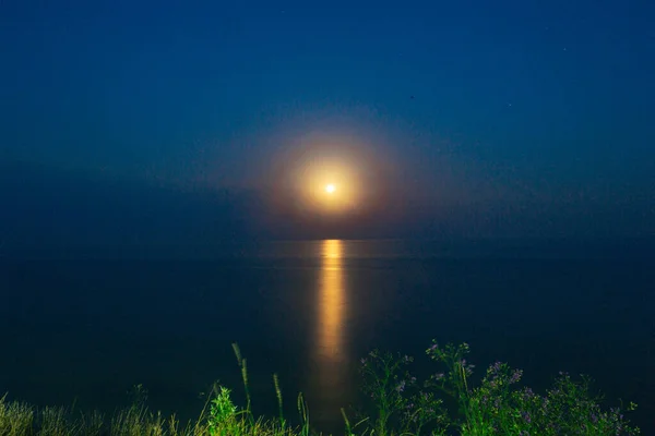 Pełnia Czerwonego Księżyca świeci jasno na niebie w ciemną noc nad spokojnym morzem. Piękna ścieżka księżycowa na wodzie — Zdjęcie stockowe