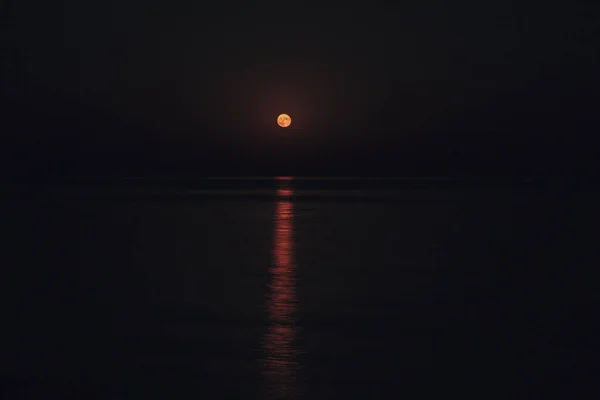 Полная Красная Луна ярко светит в небе в темную ночь над спокойным морем. Лунный путь на воде — стоковое фото