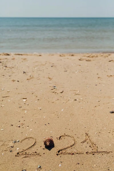 Texto 2021 Escrito en la arena de una playa. El mar sobre un fondo de letras —  Fotos de Stock