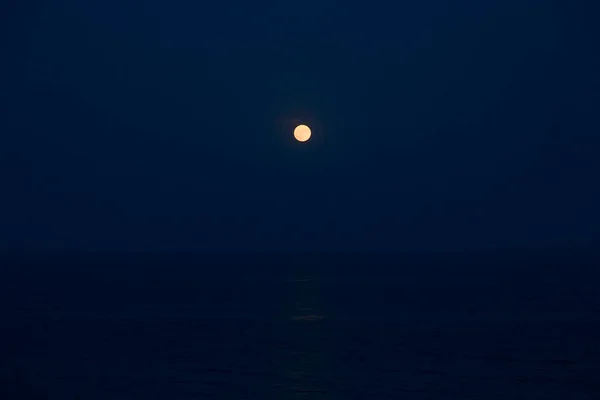 La pleine lune rouge brille brillamment dans le ciel bleu lors d'une soirée sur la mer — Photo