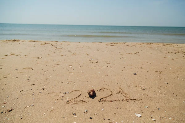 Texto 2021 Escrito en la arena de una playa. El mar sobre un fondo de letras —  Fotos de Stock