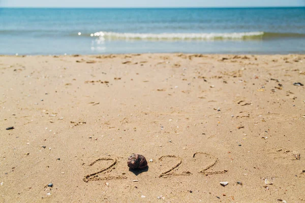 Texto 2022 Escrito en la arena de una playa. El mar sobre un fondo de letras —  Fotos de Stock