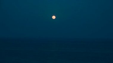 Dolunay, durgun denizin üzerindeki karanlık bir gecede gökyüzünde ışıldıyor. Su üzerindeki güzel ay yolu