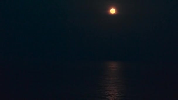 Der Vollmond leuchtet hell am Himmel in einer dunklen Nacht über dem ruhigen Meer. Schöner Zeitraffer-Mondpfad auf dem Wasser — Stockvideo