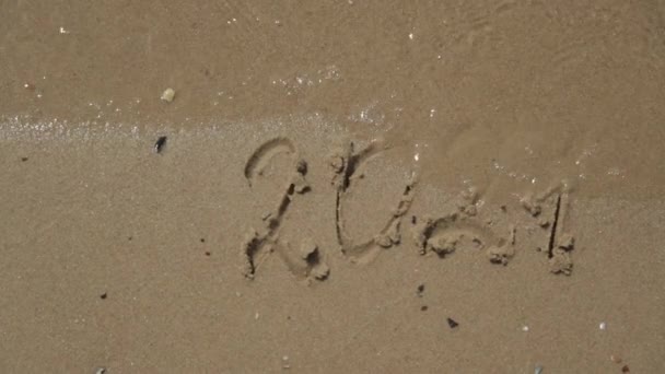 Texto 2021 Escrito en la arena de una playa. El mar sobre un fondo de letras — Vídeo de stock