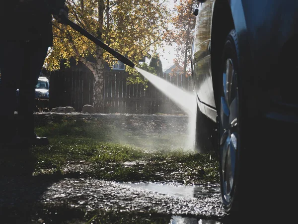 the girl washes the car at home near the garage using a pressure washer