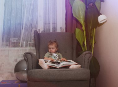 Küçük kız bir sandalyede otururken kitap sayfalarını karıştırıyor.