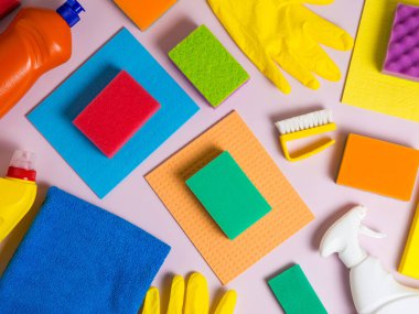 Mor arka plana yerleştirilmiş temizlik aletleri, paçavralar, süngerler, şişeler ve eldivenler