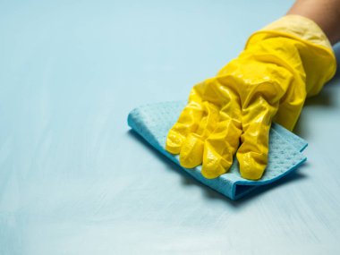 Sarı lastik eldivenli bir el mavi arka planda sabunlu köpüklü bir temizlik süngeri tutar. Ev temizliği konsepti, temizlik hizmeti