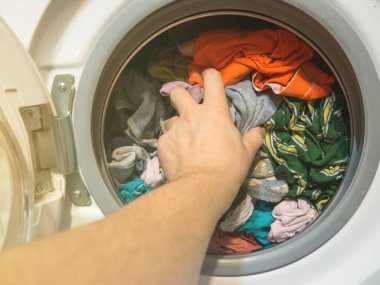 Adam çamaşır makinesine çamaşır koyar, yakın plan.