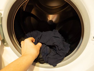 Adam çamaşır makinesine çamaşır koyar, yakın plan.