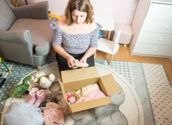 Winter baby clothes donation concept. Woman preparing used old clothes at home.