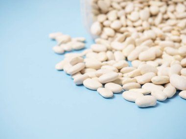 Mavi bir masanın üzerindeki plastik bir konteynırdan saçılmış kuru beyaz fasulyeler. Boşluğu kopyala