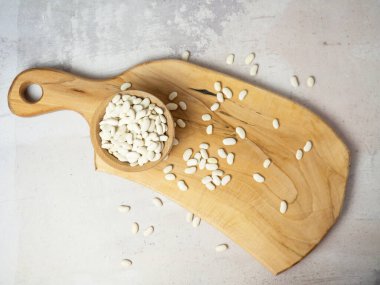 Tahta bir fincanda beyaz fasulyeler ve kaşıklar masaya saçılmış.