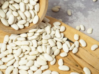 Tahta bir fincanda beyaz fasulyeler ve kaşıklar masaya saçılmış.