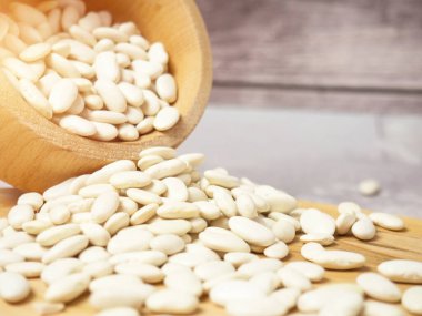 Tahta bir fincanda beyaz fasulyeler ve kaşıklar masaya saçılmış.