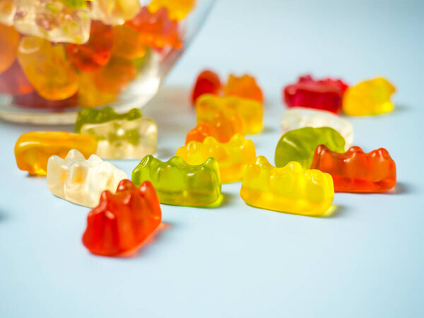 Bowl with tasty bright gummy bears on blue table