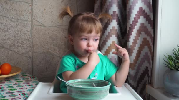 Egy Zöld Ruhás Kislány Leül Egy Etetőszékhez Asztalról Eszi Babakását — Stock videók