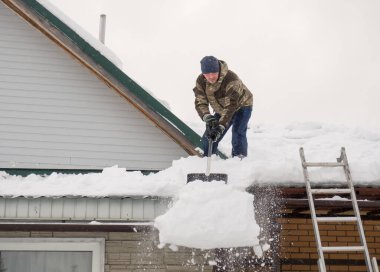 Bir adam karla kaplı bir evin çatısından kürekle kar kaldırıyor. Kar fırtınasından sonra bir sürü taze kar, zor ve tehlikeli iş.