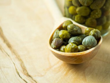 Tahta bir kaşıkta salamura edilmiş yeşil kapari. Yaklaş, seçici odaklanma.