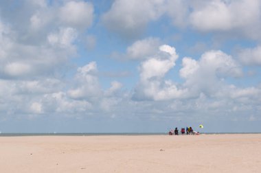 Açık mavi gökyüzü ve denizin üzerinde beyaz dinamik bulutlar, grisont manzarası, kumsalın ince kenarı.