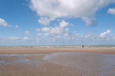 Açık mavi gökyüzü ve denizin üzerinde beyaz dinamik bulutlar, grisont manzarası, kumsalın ince kenarı.