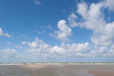 Açık mavi gökyüzü ve denizin üzerinde beyaz dinamik bulutlar, ufuk, kumsalın ince kenarı