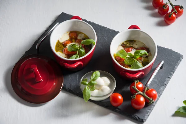 Italian caprese salad, baked cherry tomatoes, mozzarella and basil on a white table, still life — Stock Photo, Image